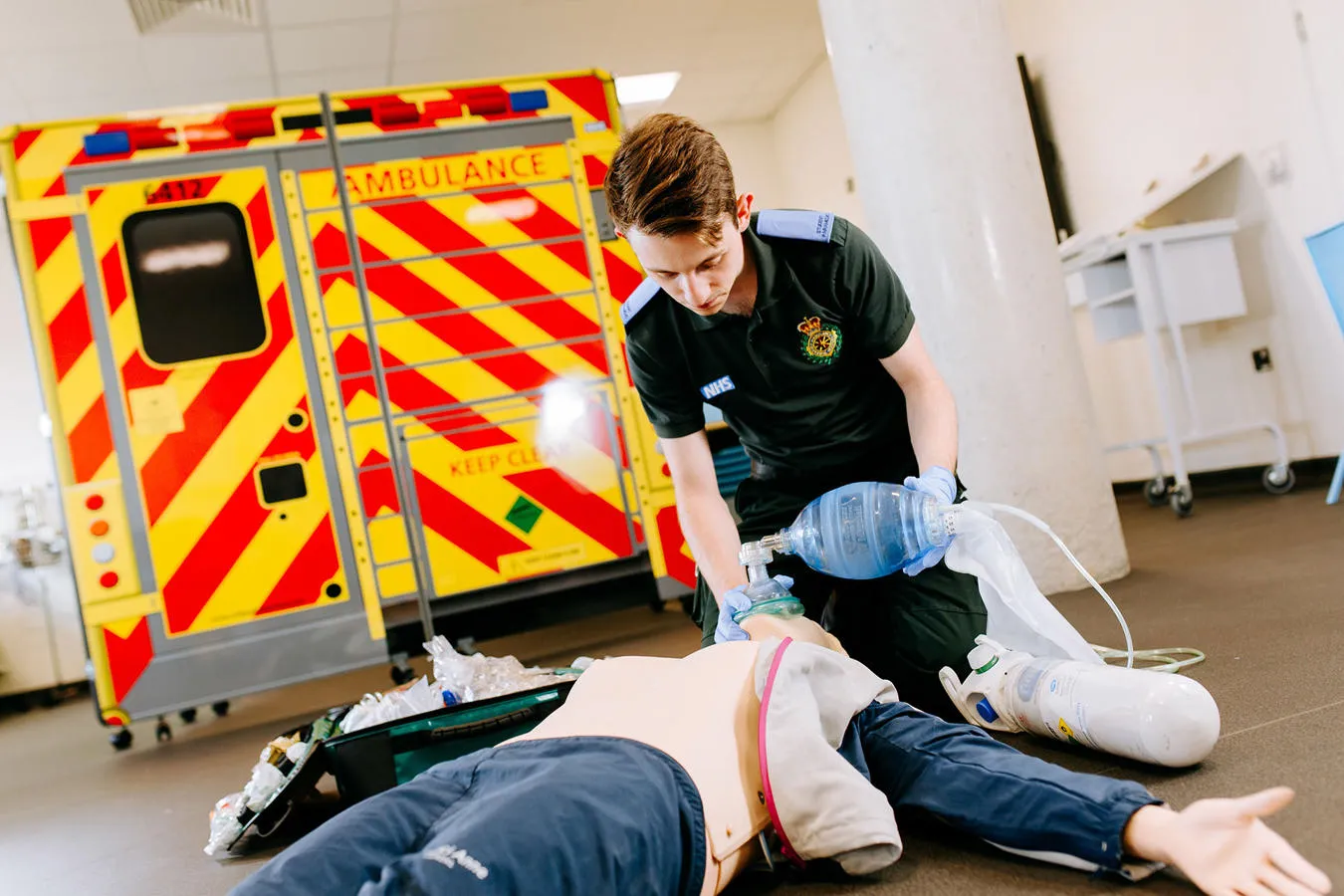 Kneeling student paramedic uses a breathing mask on a mannequin