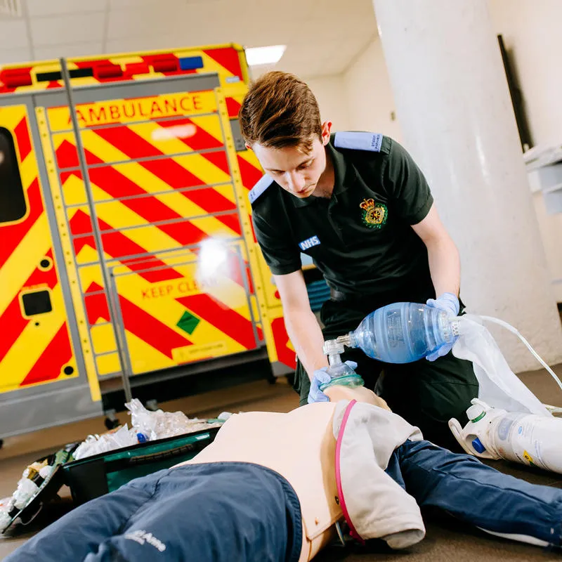 Kneeling student paramedic uses a breathing mask on a mannequin