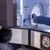 A doctor monitors a scan on a computer while in the background a patient enters an MRI scanning machine