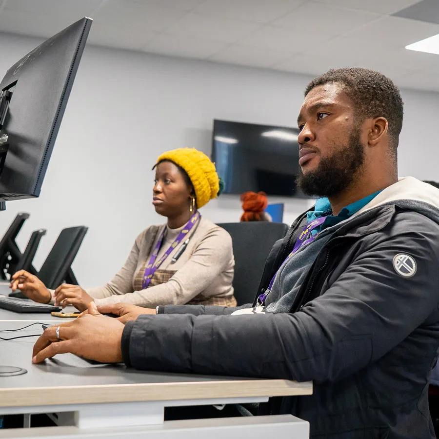 A man and a woman siting infront of a computer typing