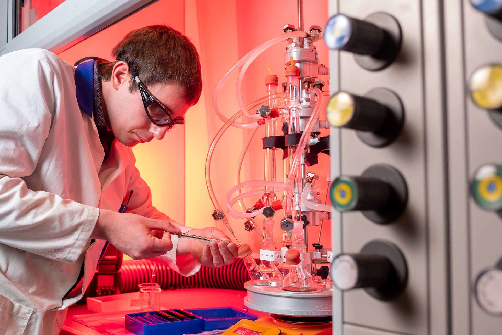 A man in a lab coat is working intently on a machine, surrounded by laboratory equipment and tools.