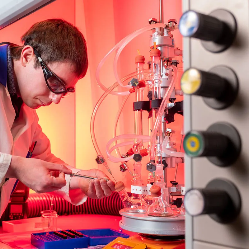A man in a lab coat is working intently on a machine, surrounded by laboratory equipment and tools.