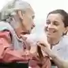 A student nurse smiling at an elderly patient while holding her hand