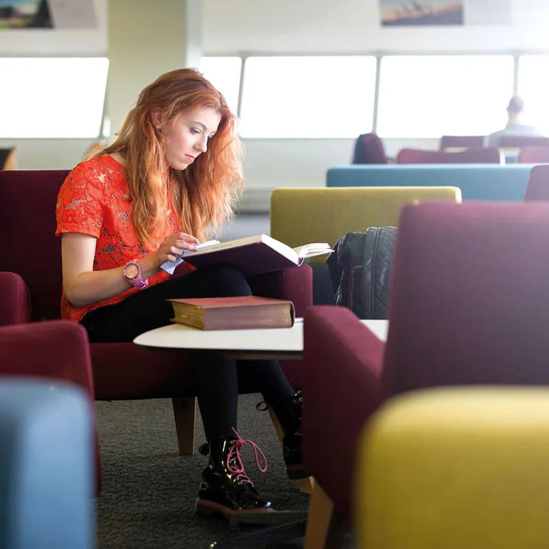 student reading books in a library seating area