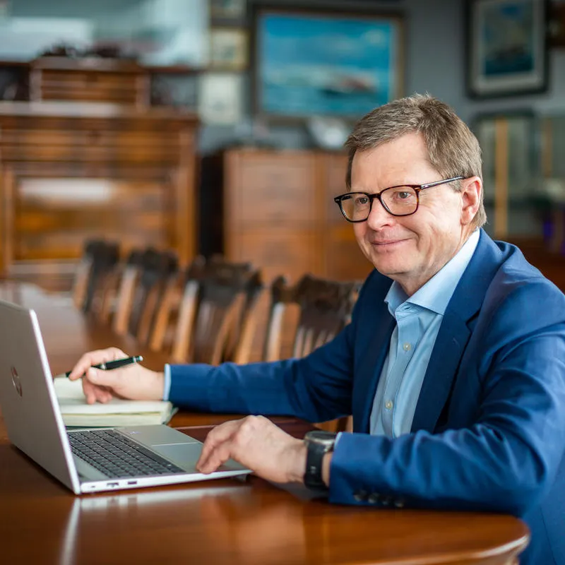 Man in suit sitting at a table with an open laptop and notebook