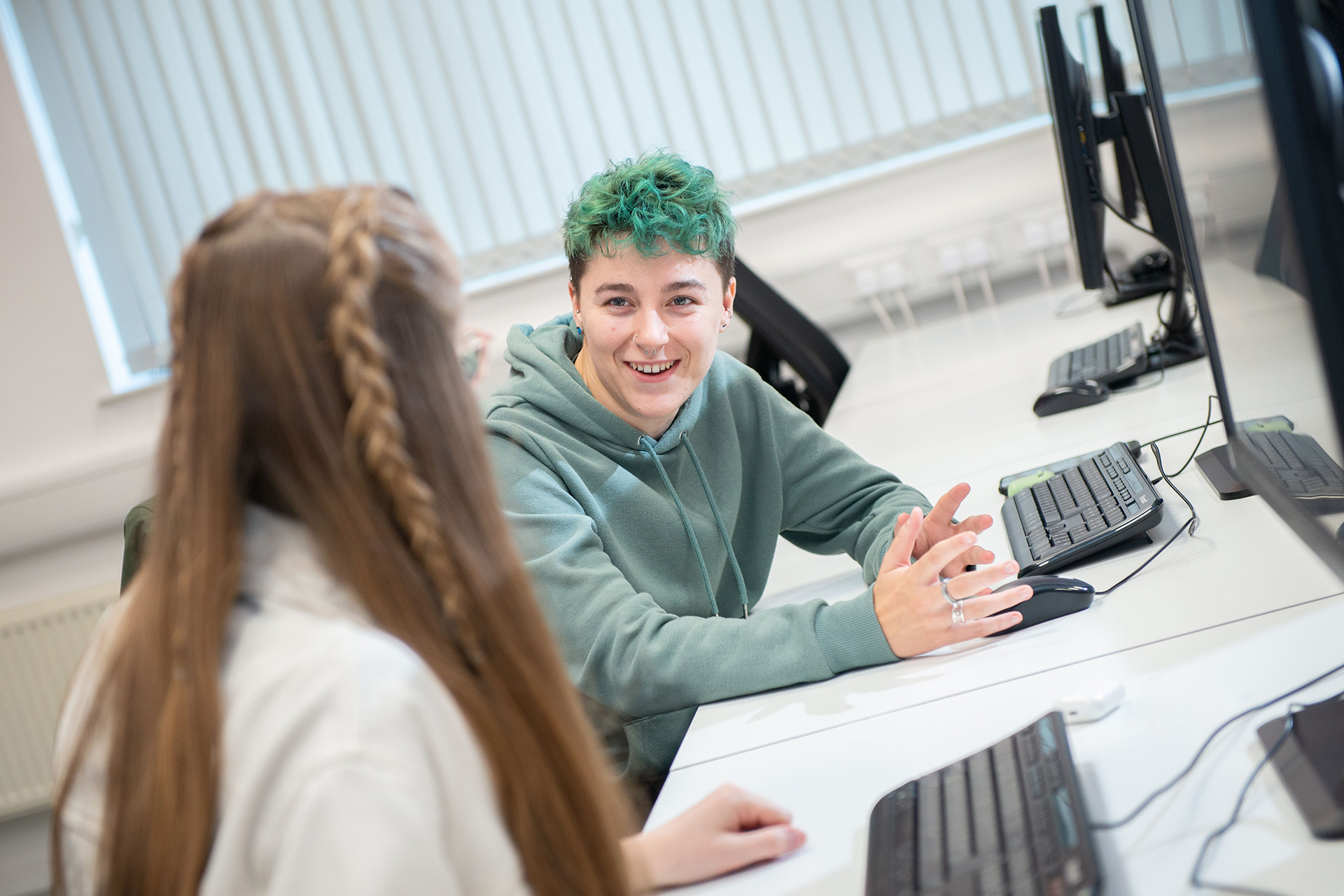 Two students discussing and laughing at a computer bank.