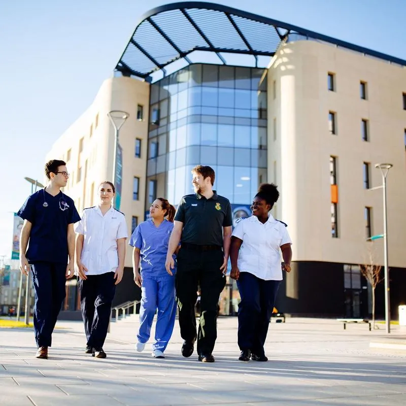 Health Students wearing a variety of NHS uniforms walking by the Allam Medical Building