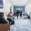 Some students relax in chairs while others walk past them in a modern business school corridor