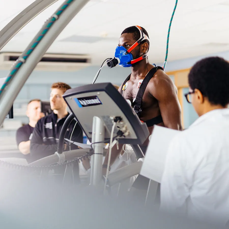 A man with a mask on a treadmill undergoing tests with a man in a white lab coat standing by