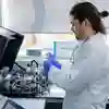 A man in a lab coat operates a complex machine in a laboratory setting.