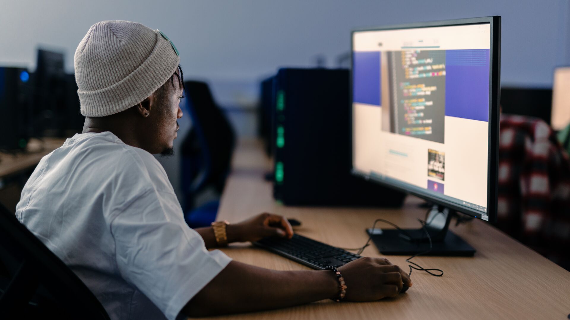 Student waring a beanie hat sitting at a desk working on a high speed computer