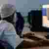 Student waring a beanie hat sitting at a desk working on a high speed computer
