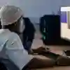 Student waring a beanie hat sitting at a desk working on a high speed computer