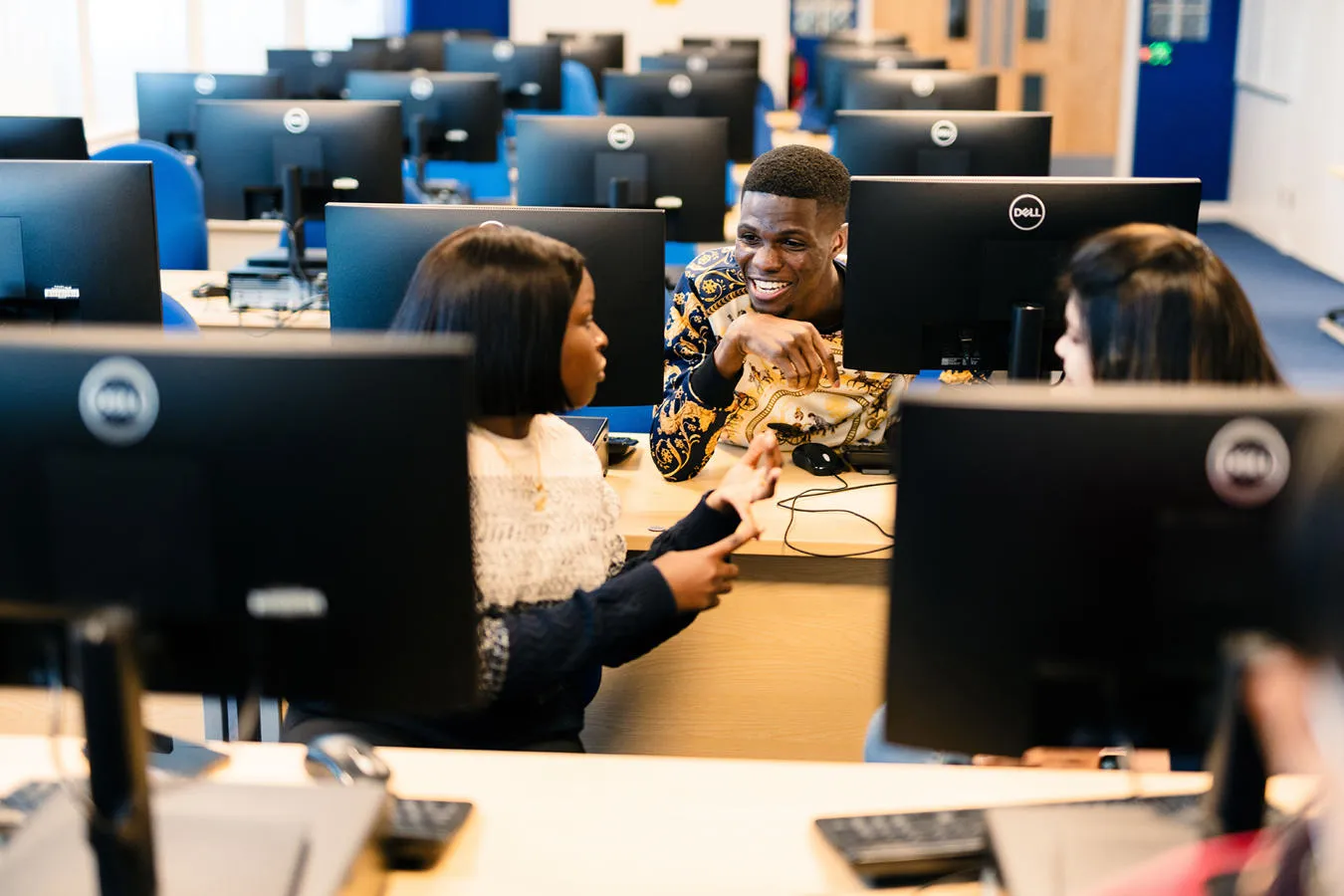 Three students talk while seated at terminals in the Computer Science SuperLab