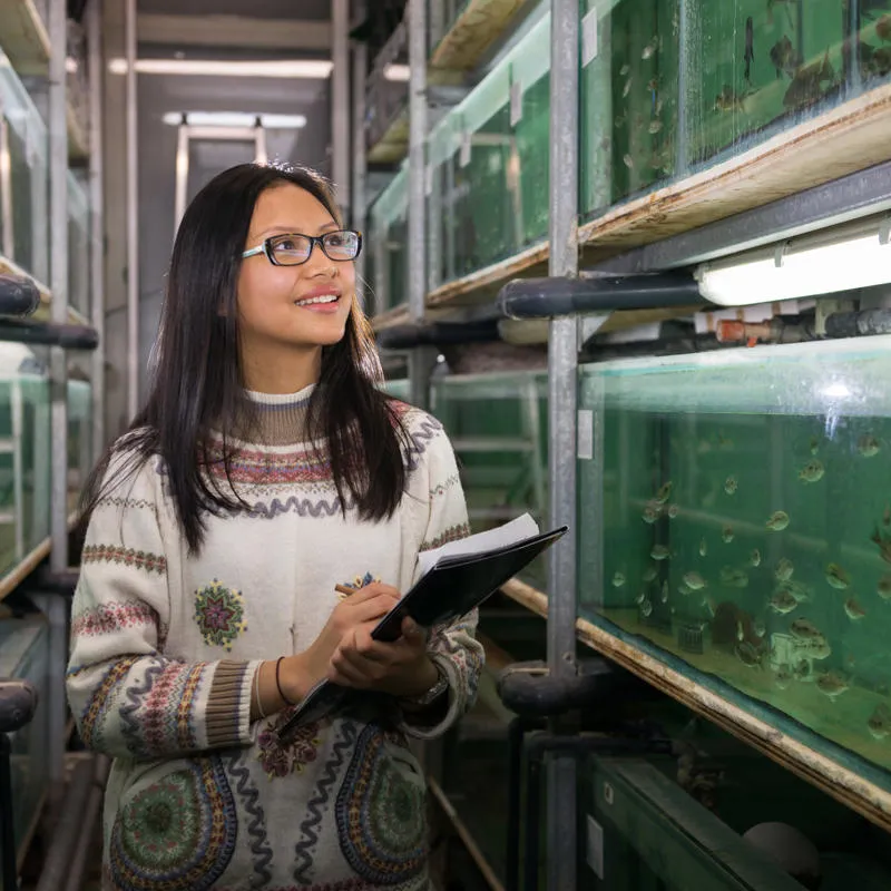 An Environmental Science student looking at marine life in a tank while making notes