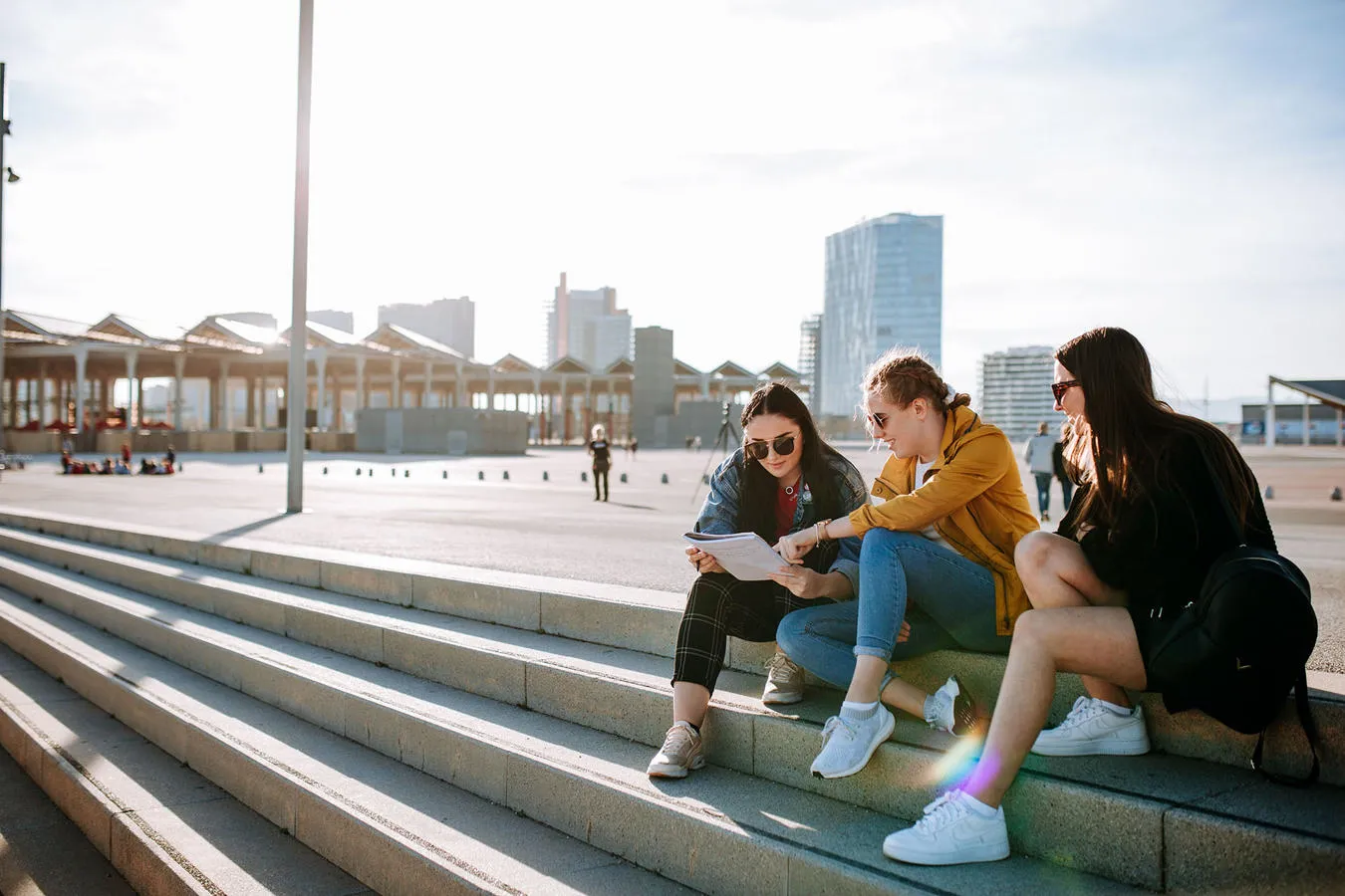 Three students seated on steps point to a book