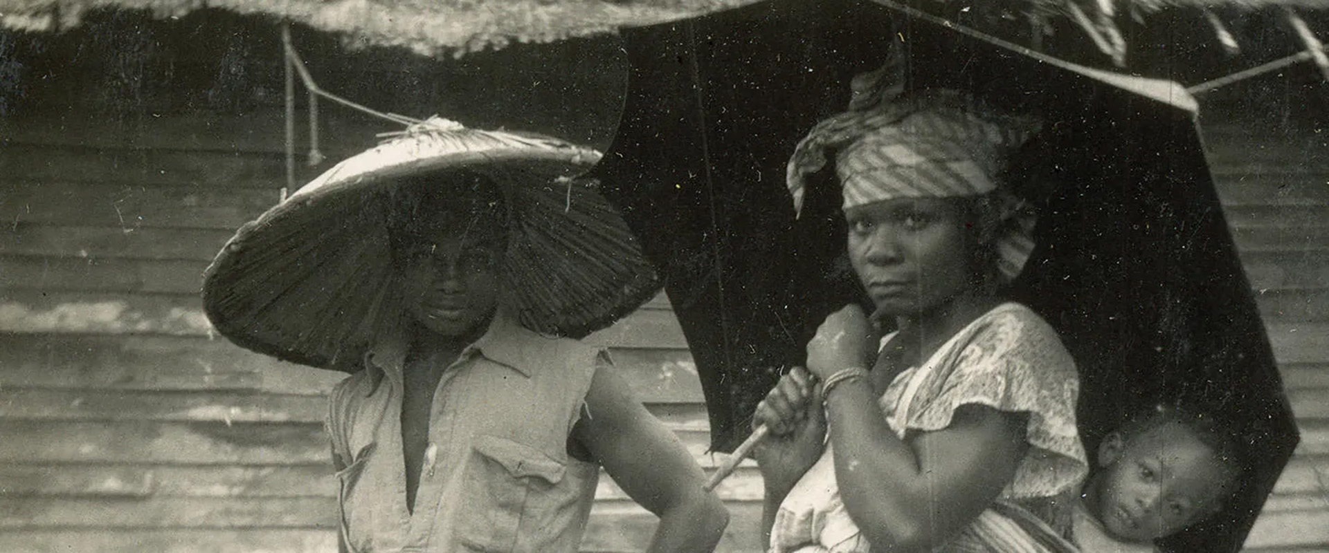 Black and white photograph of two women carrying umbrellas, one with a child strapped to her back 