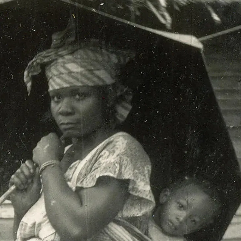 Black and white photograph of two women carrying umbrellas, one with a child strapped to her back