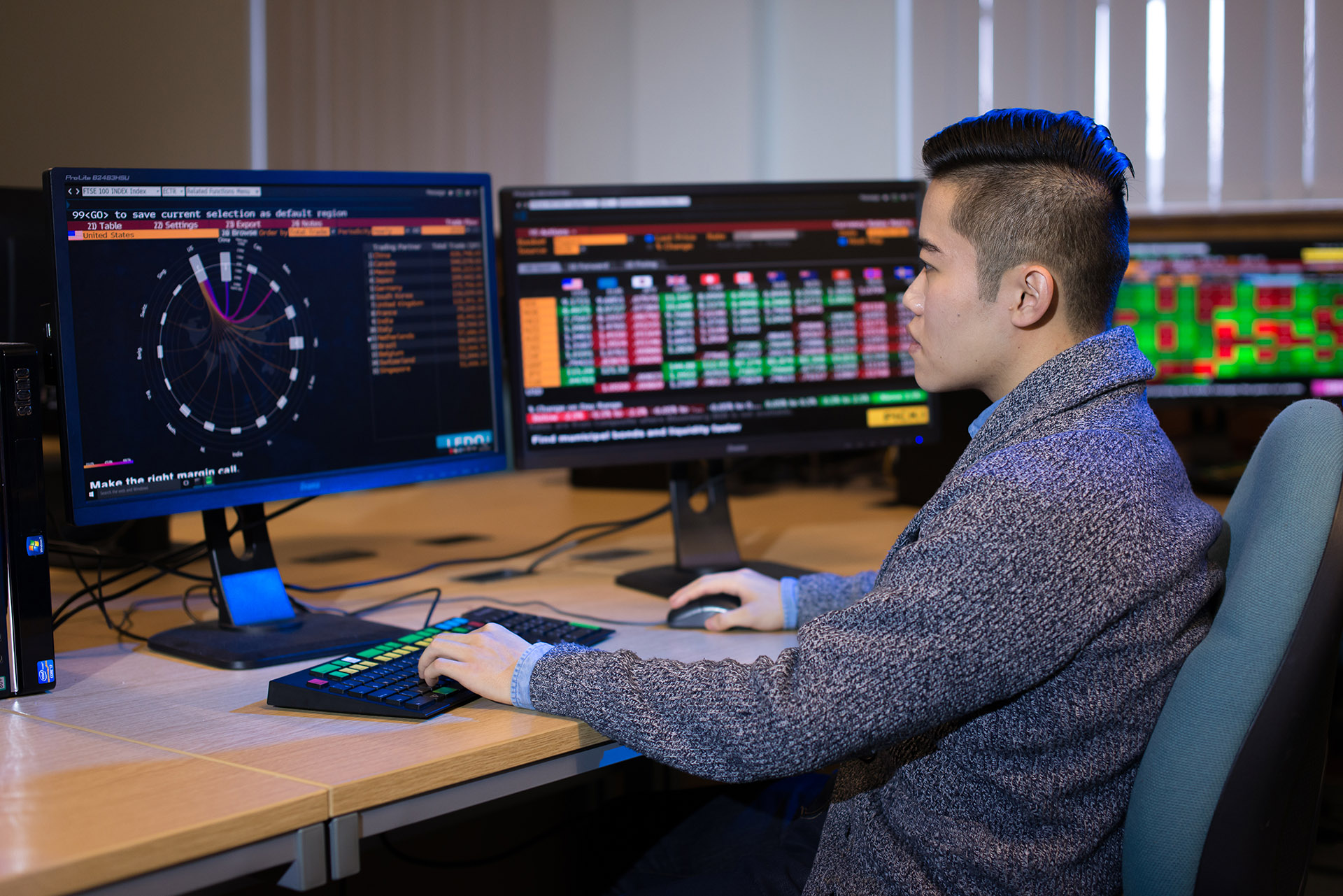 Student sitting at desk with several computer monitors in the Bloomberg suite