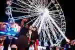 A group of students taking a selfie infront of an illuminated ferris wheel at night