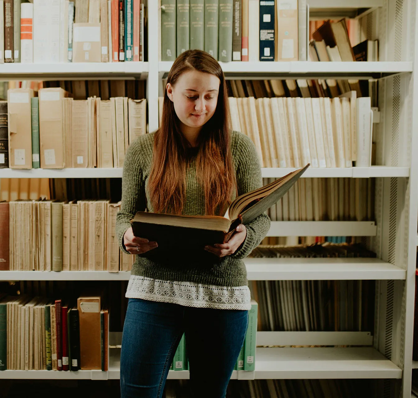 A students reads a book in front of library shelves