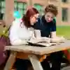 Male and female students sitting at a picnic table looking at a brochure