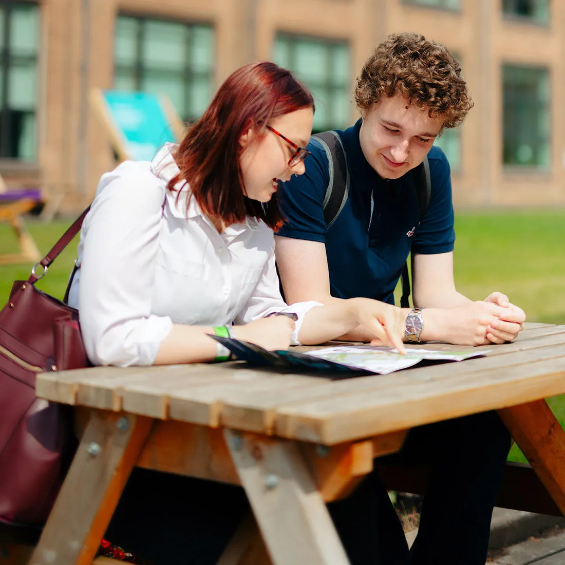 Male and female students sitting at a picnic table looking at a brochure