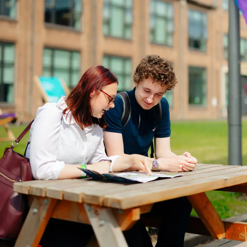 Male and female students sitting at a picnic table looking at a brochure