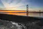 Humber Bridge at sunset and the foreground showing muddy, grassy riverbank.