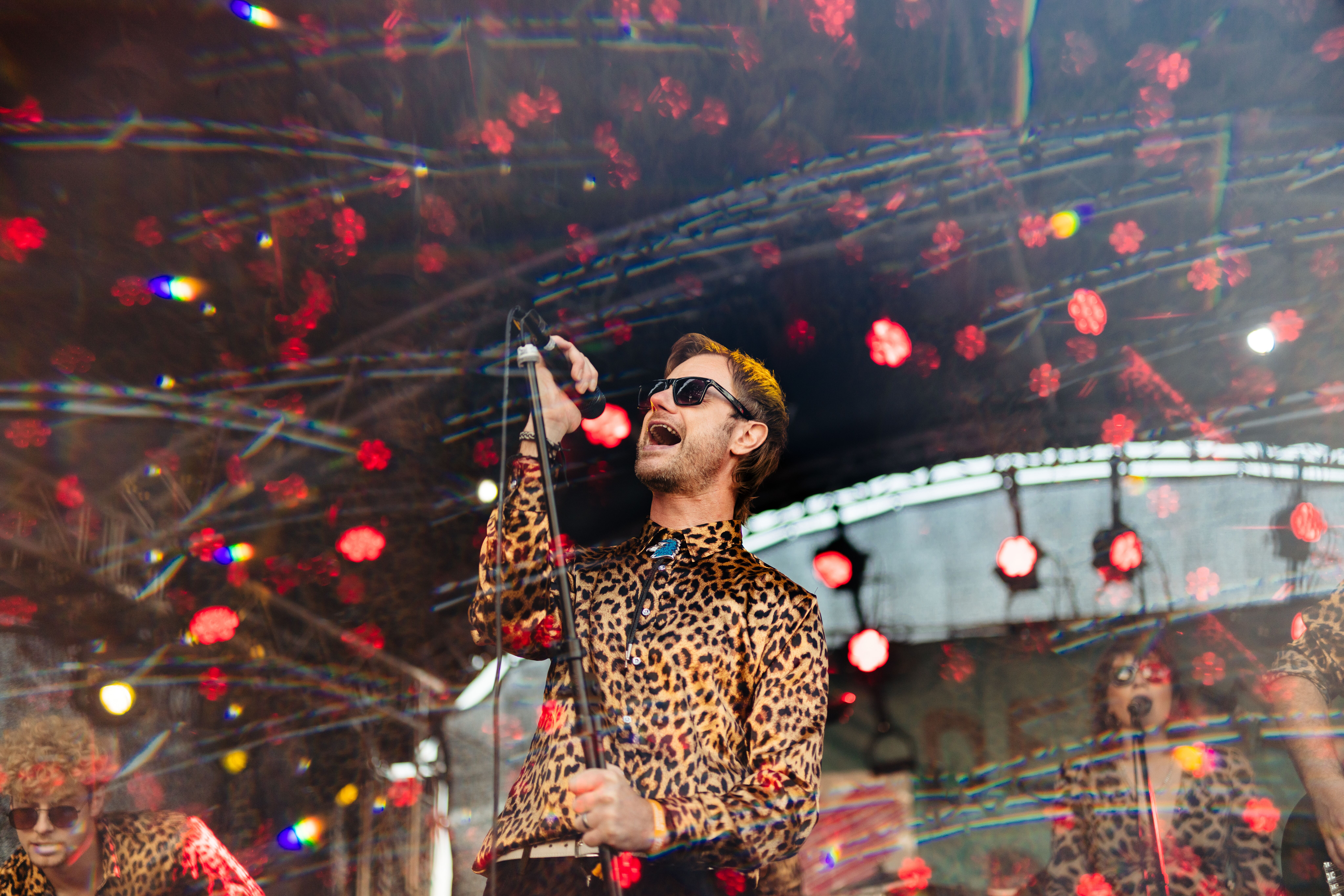 A singer wearing a leopard print shirt and sunglasses screams into a microphone at Humber Street Sesh