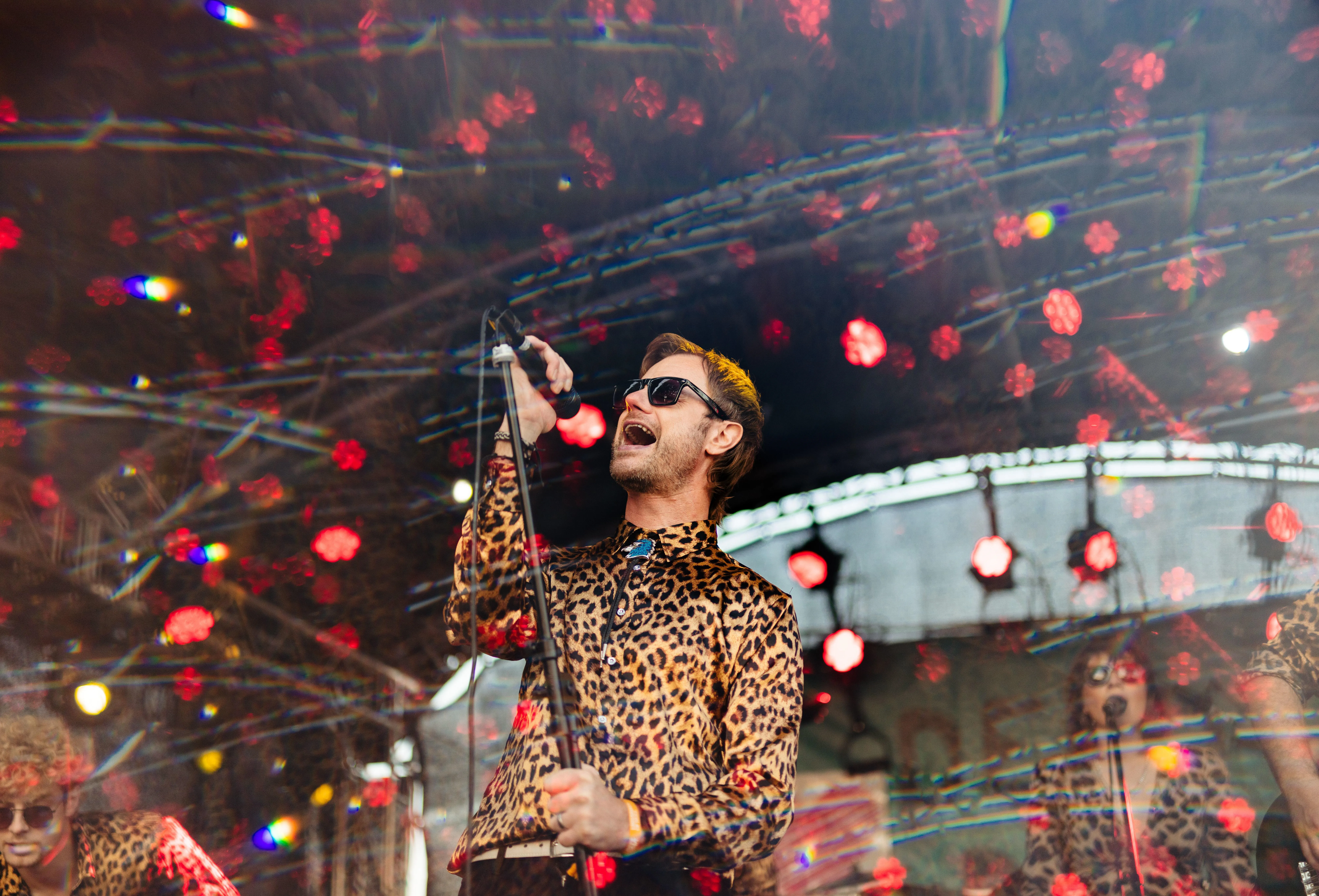 A singer wearing a leopard print shirt and sunglasses screams into a microphone at Humber Street Sesh