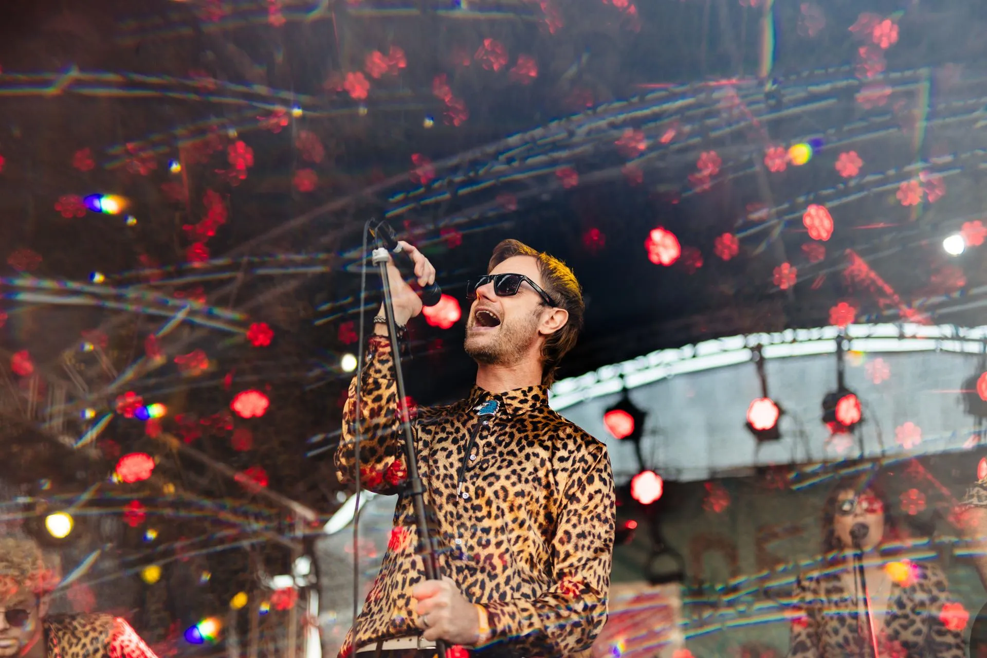 A singer wearing a leopard print shirt and sunglasses screams into a microphone at Humber Street Sesh