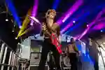 Leopard print dressed guitarist plays big red electric guitar.