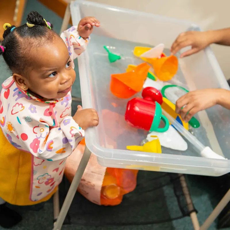 A young child wearing an apron playing in a table sand pit