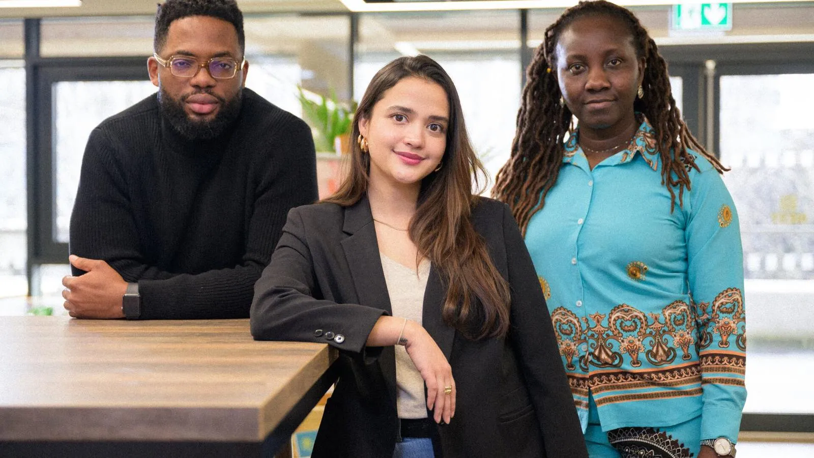 3 postgraduate students leaning against a table looking at camera with a half smile