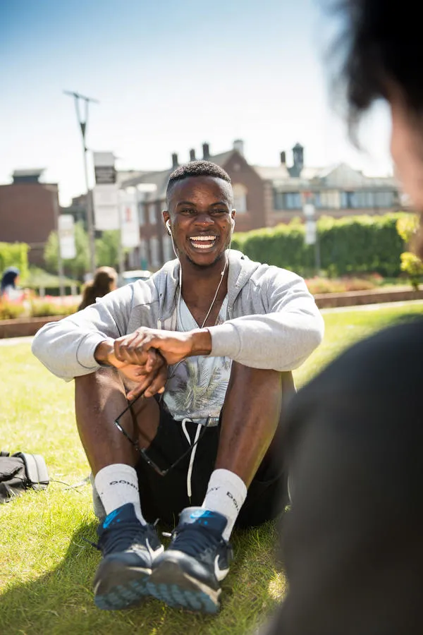 International Student sat smiling on the lawn in front of BJL Library