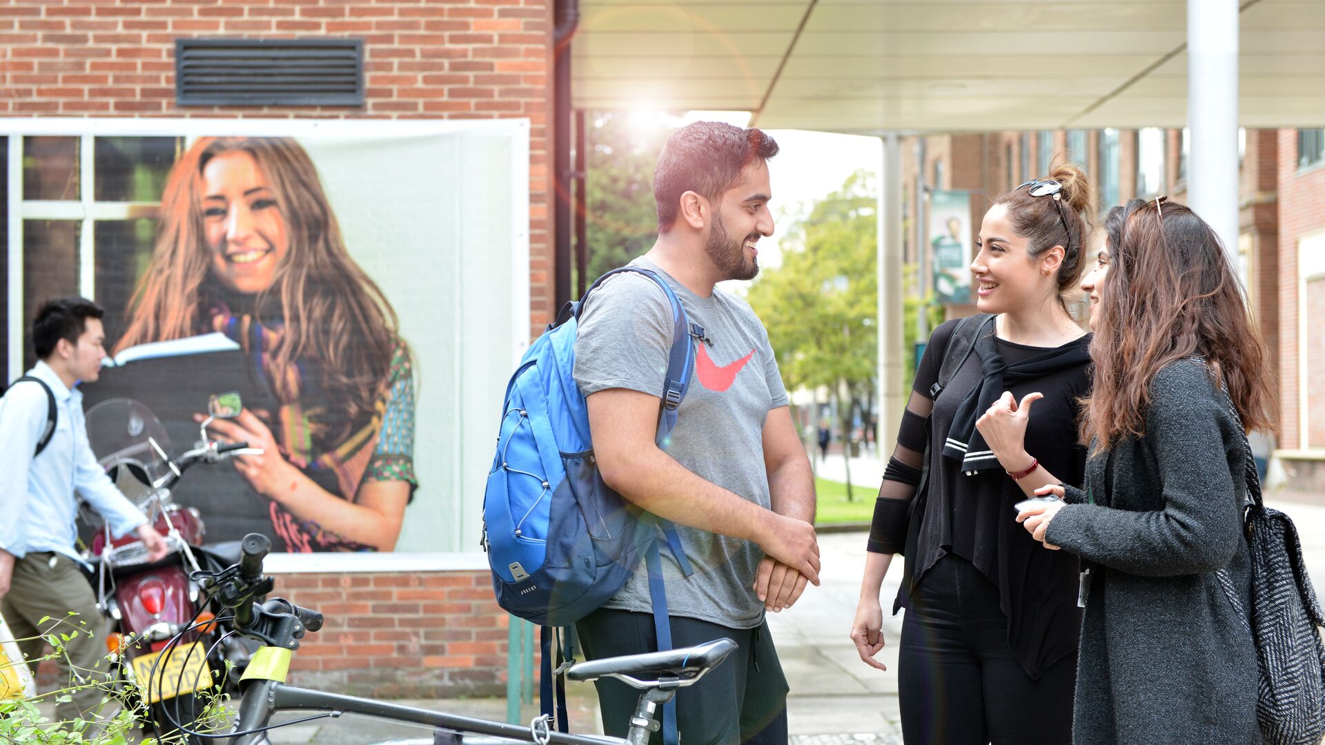 Students smiling outside buildings with a bike