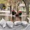A flooded street with people being rescued in a dingy with sandbanks in the forground.