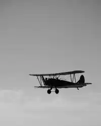 Black and white photo of an old aeroplane flying through the sky above the clouds.