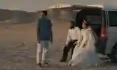 A bride and groom sit in the back of an open boot in a desert landscape