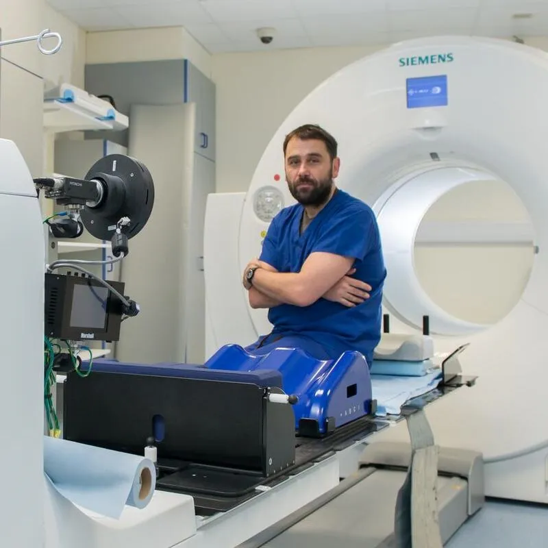 A medical professional in blue scrubs casually sits on a high tech scanning machine