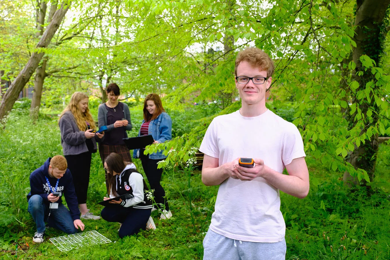 Several individuals standing together in a vibrant forest, with tall trees and foliage in the background.