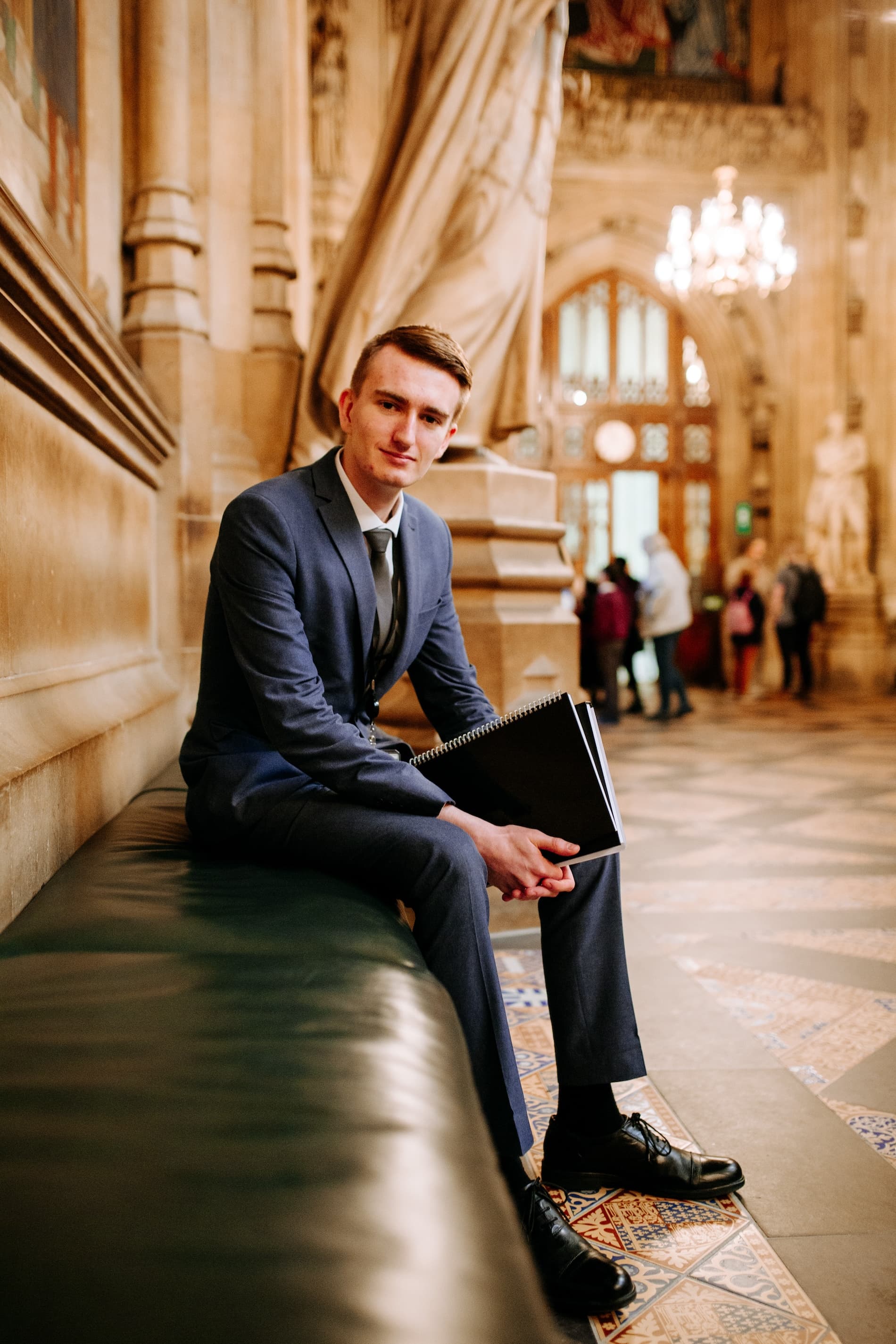Hull student James Parker wearing a smart suit and sitting on a bench inside the Houses of Parliament.