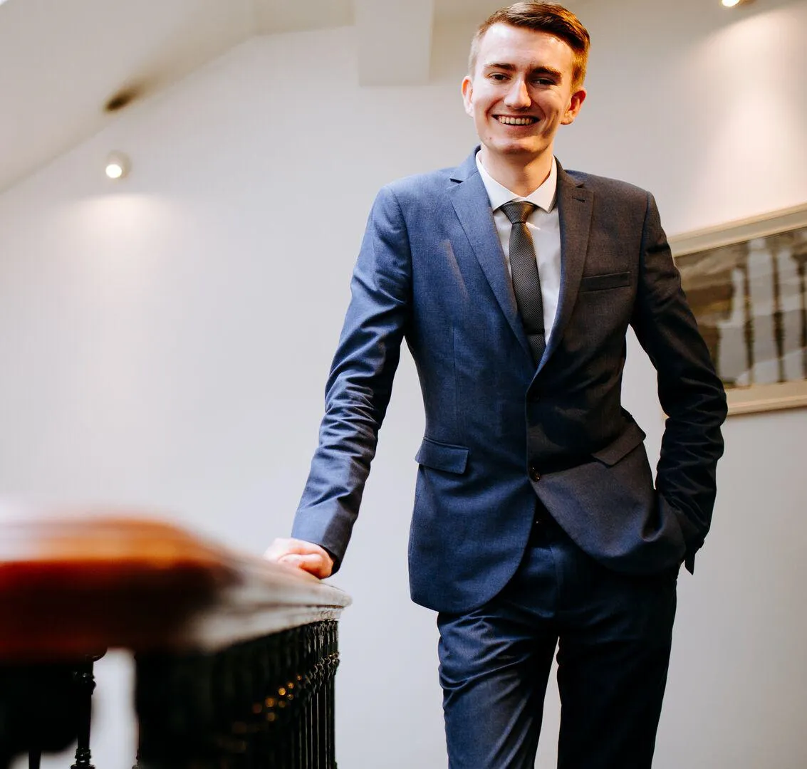 Smartly-dressed Politics student, James Parker, casually leaning and smiling to the camera while on placement at Westminster.