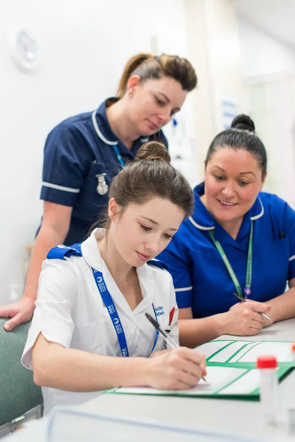 A group of health students stand around a desk in a mock hospital ward