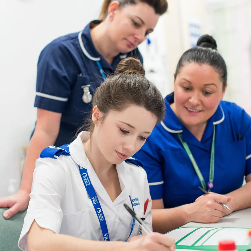 A group of health students stand around a desk in a mock hospital ward