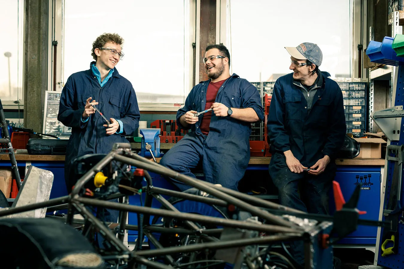 Three students in mechanic's overalls standing in a workshop 
