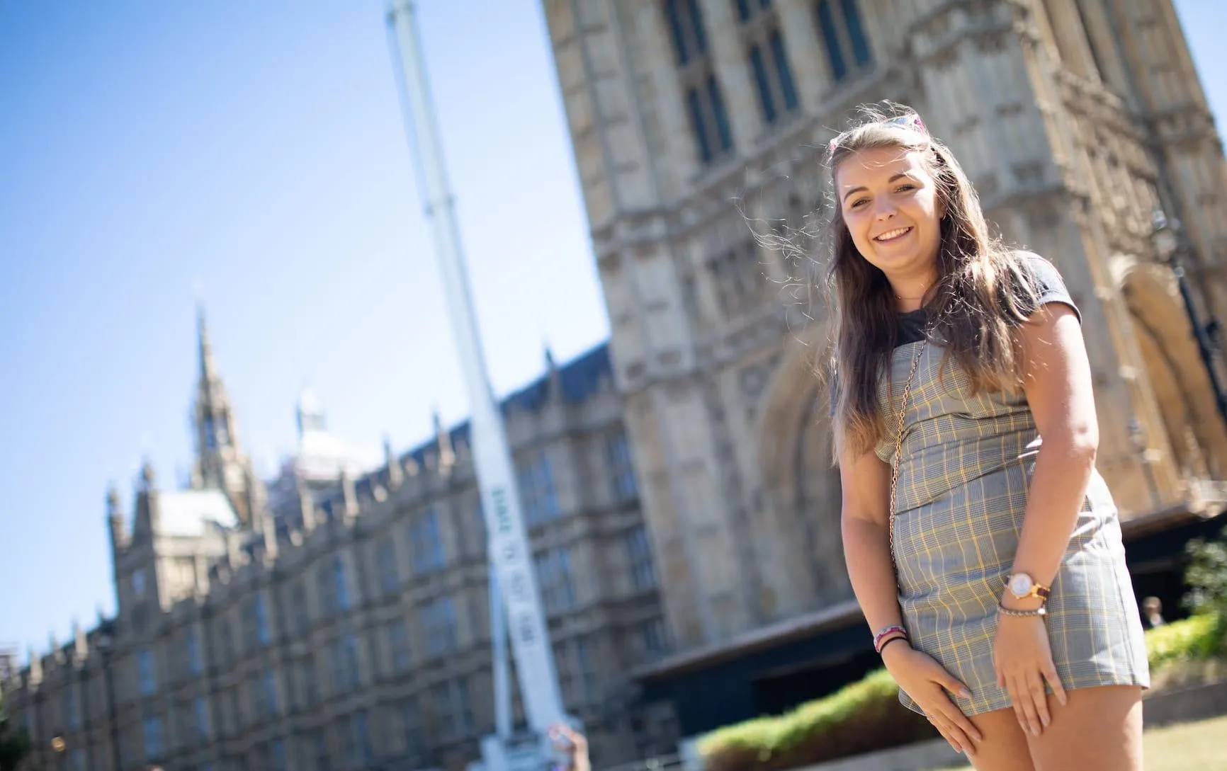 A female Hull Politics student with long brown hair stands smiling outside the Palace of Westminster on a sunny day