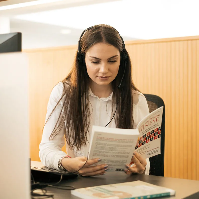 A student sitting at a desk wearing headphones and reading