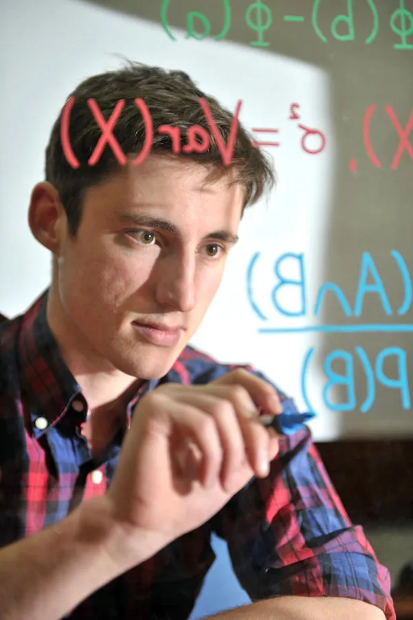 A maths student writing equations on clear glass whiteboard